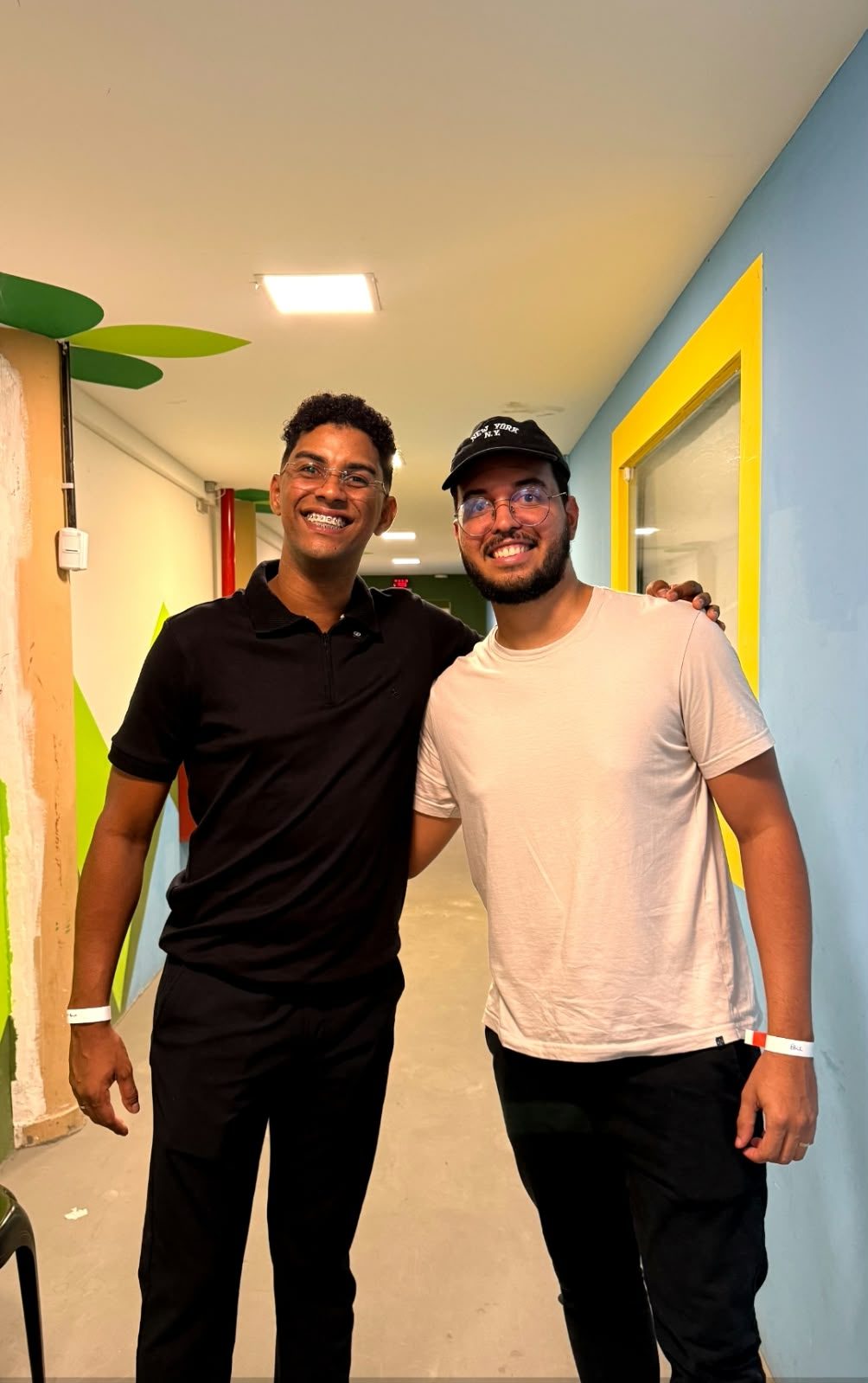 Dois homens sorrindo abraçados num corredor
